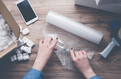 A person packing fragile glassware into bubble wrap