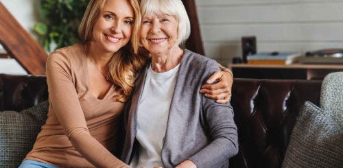 Portrait of elderly mother and middle aged daughter smiling together on the couch at home