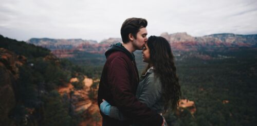 Romantic moment captured: A young couple sharing a kiss with a breathtaking view in the background.