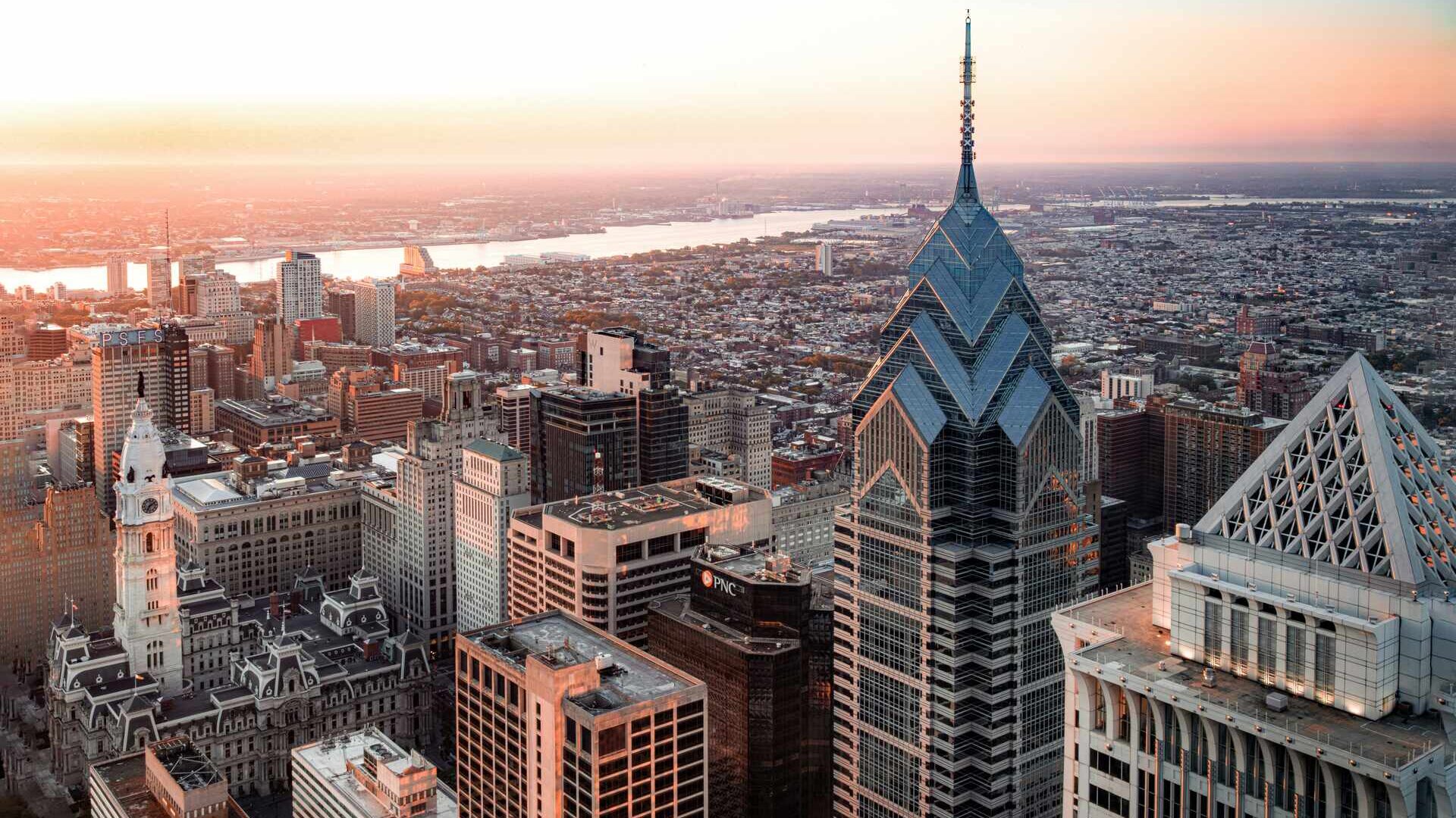 Aerial view of Philadelphia, showcasing the cityscape under a vast sky. Skyscrapers, historic landmarks, and urban architecture blend together in this dynamic skyline, capturing the essence of Philadelphia from a bird's-eye perspective.