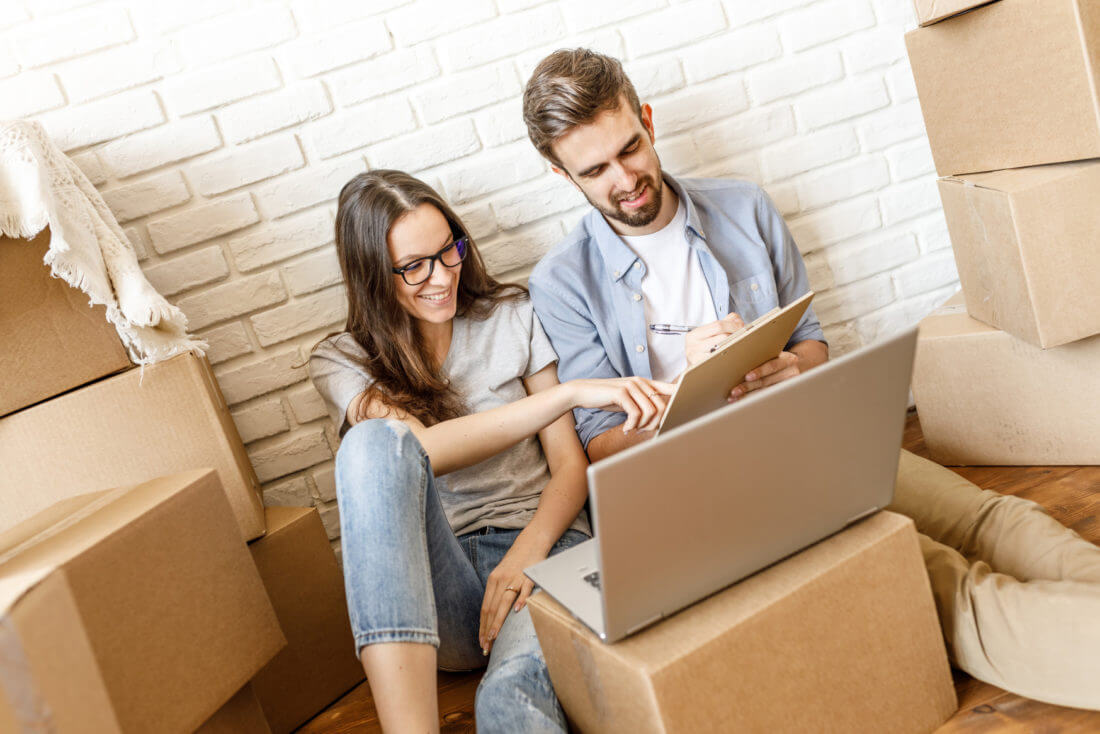 Couple surrounded by boxes looking at a checklist and a laptop