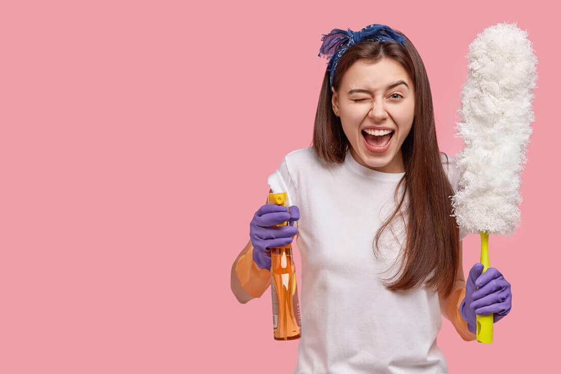 Woman smiling and winking while holding cleaning supplies
