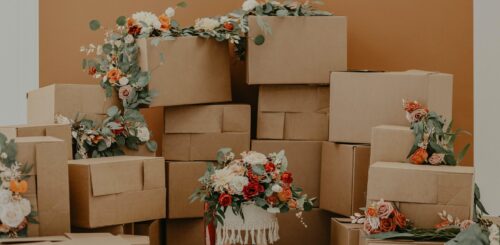 Boxes juxtaposed with vibrant flowers, a scene of transition and renewal. The boxes represent the practicalities of moving, while the flowers symbolize the fresh beginnings and a touch of beauty amidst the process of change.