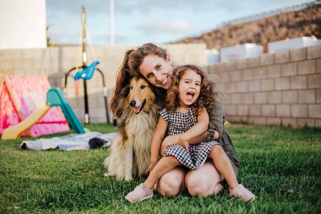 A woman hugging a dog and a girl in a backyard