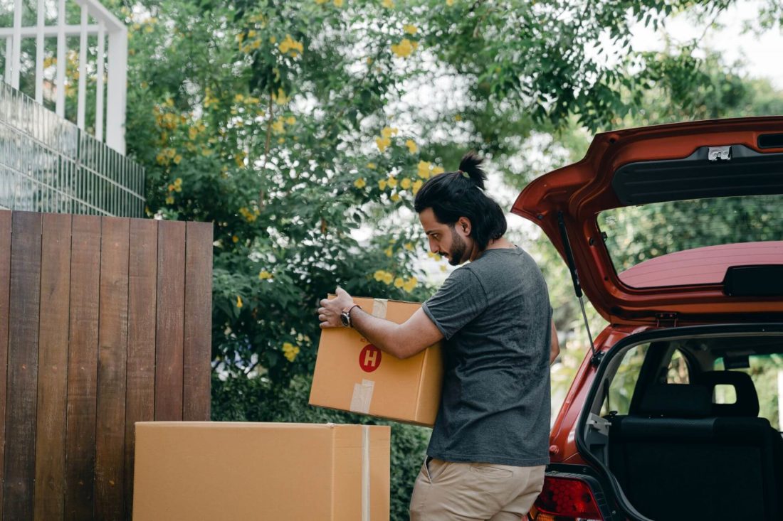 A man putting boxes in the back of a car before long-distance movers near him come to pack other stuff