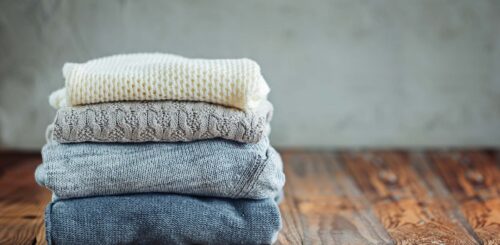 Pile of knitted winter clothes on wooden background, sweaters, space for text. Toned image.