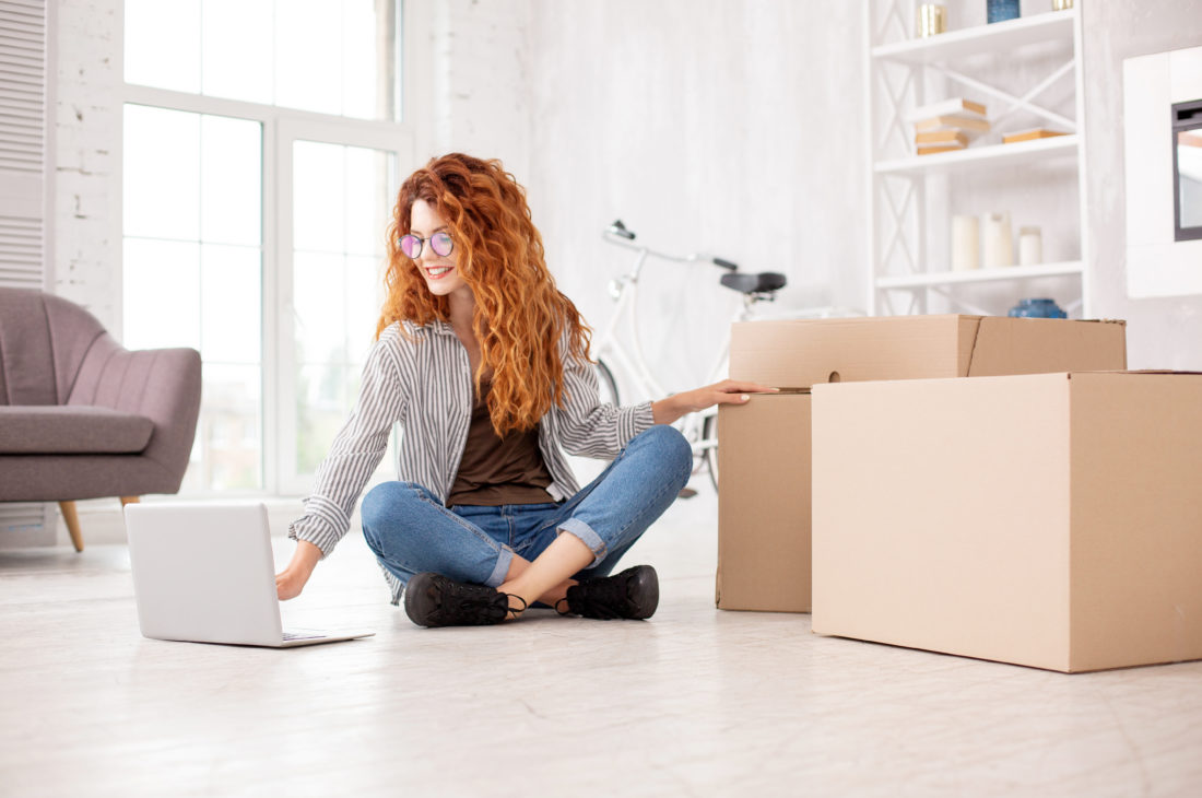 Woman sitting on the floor booking cross-country moving services on her laptop