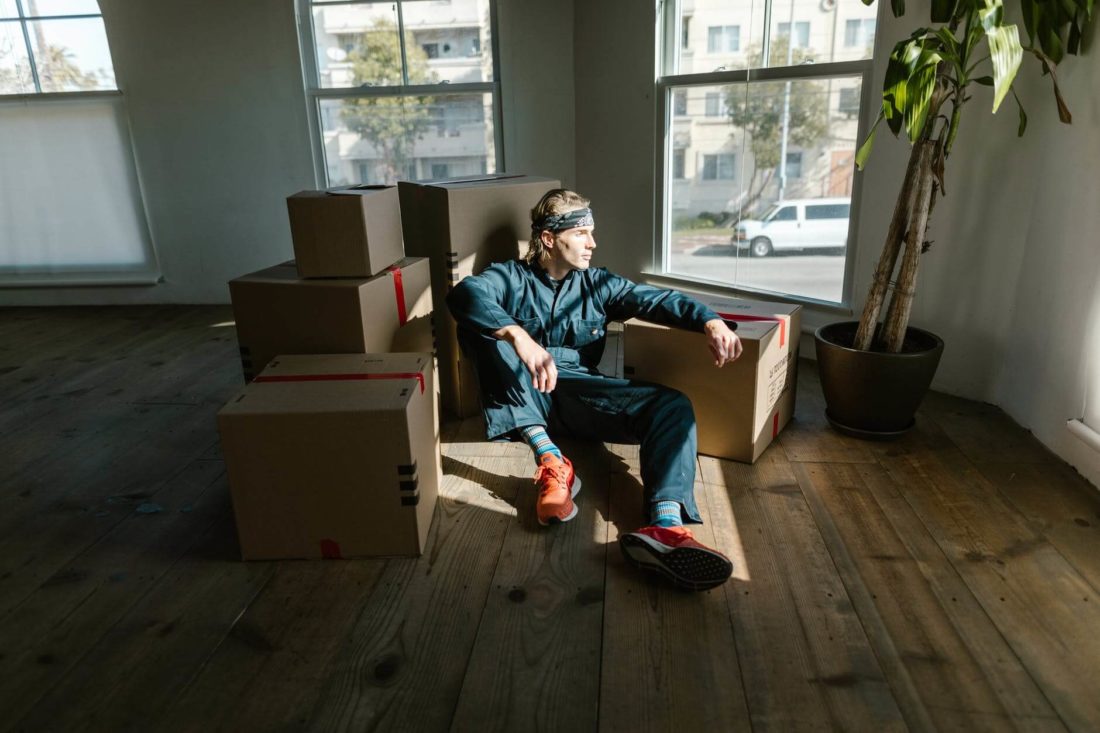 A professional cross-country mover surrounded by boxes is sitting on the floor