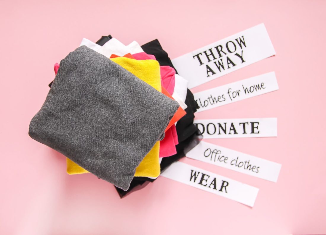 piles of clothes with labels throw away, donate, wear, to be packed for cross-country moving 
