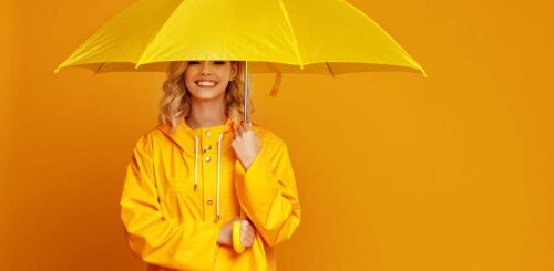 young happy emotional cheerful girl laughing with umbrella on colored yellow background
