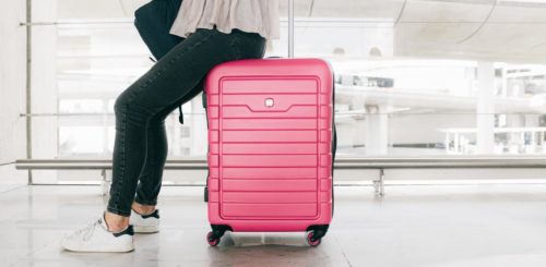 A woman is at the airport, sitting on her pink suitcase
