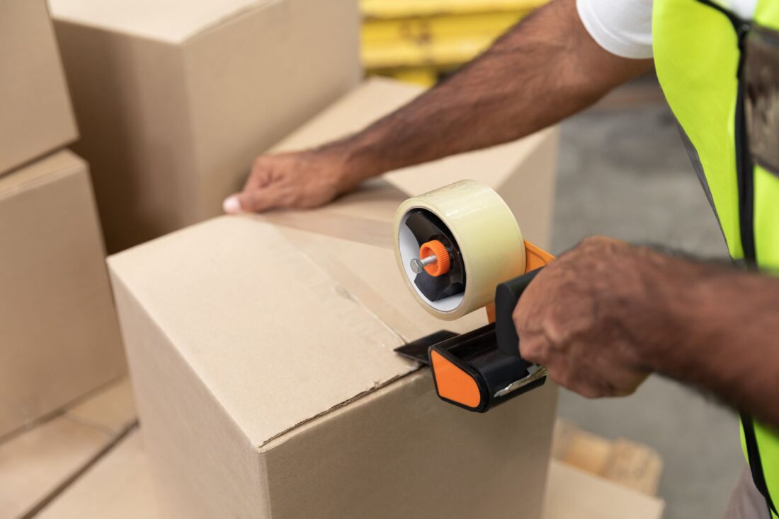 A man using tape and a dispenser to seal a box