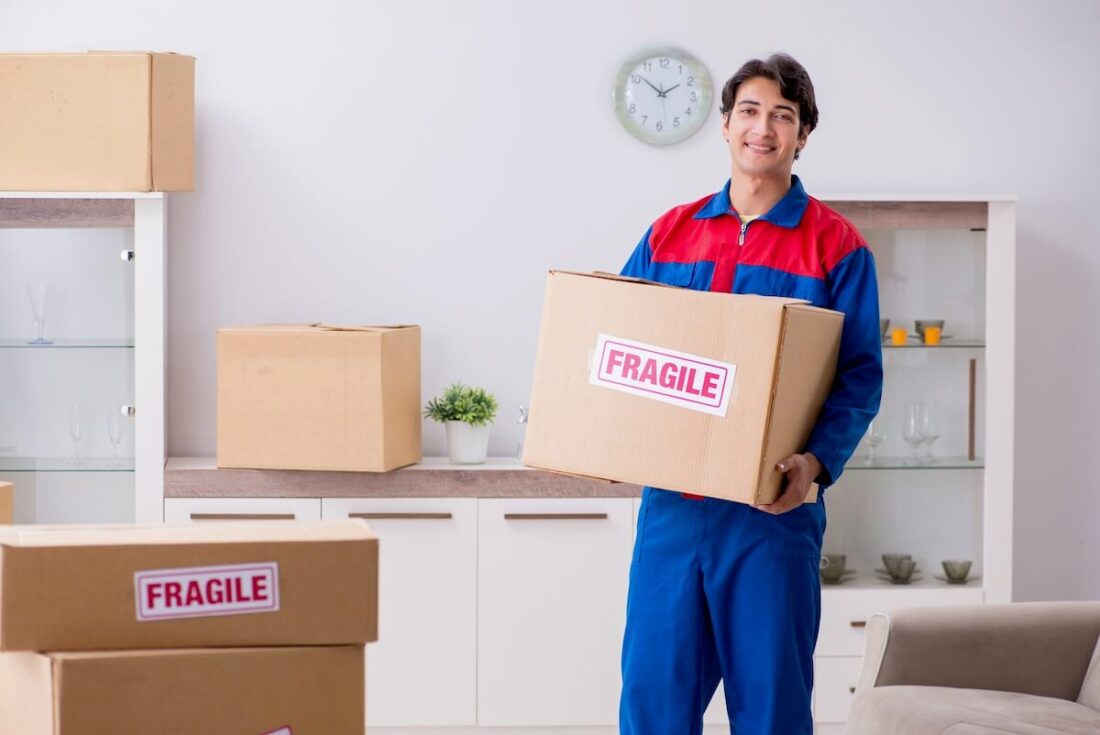 A mover carrying a box and smiling Long Distance USA Movers Logo