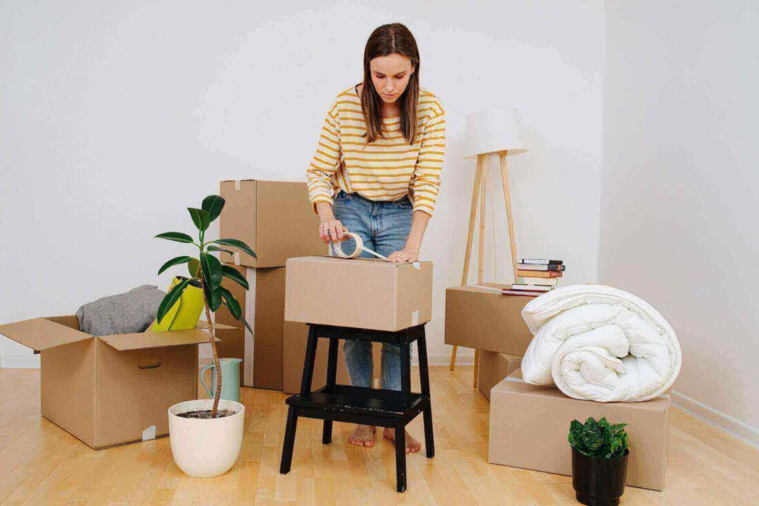 A girl sealing a box with cutlery before long-distance moving