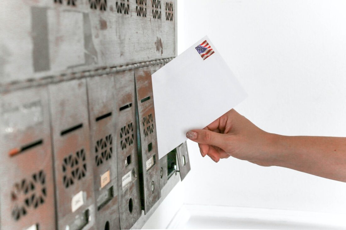 A person off-screen putting an envelope with an American flag stamp into a P.O. box