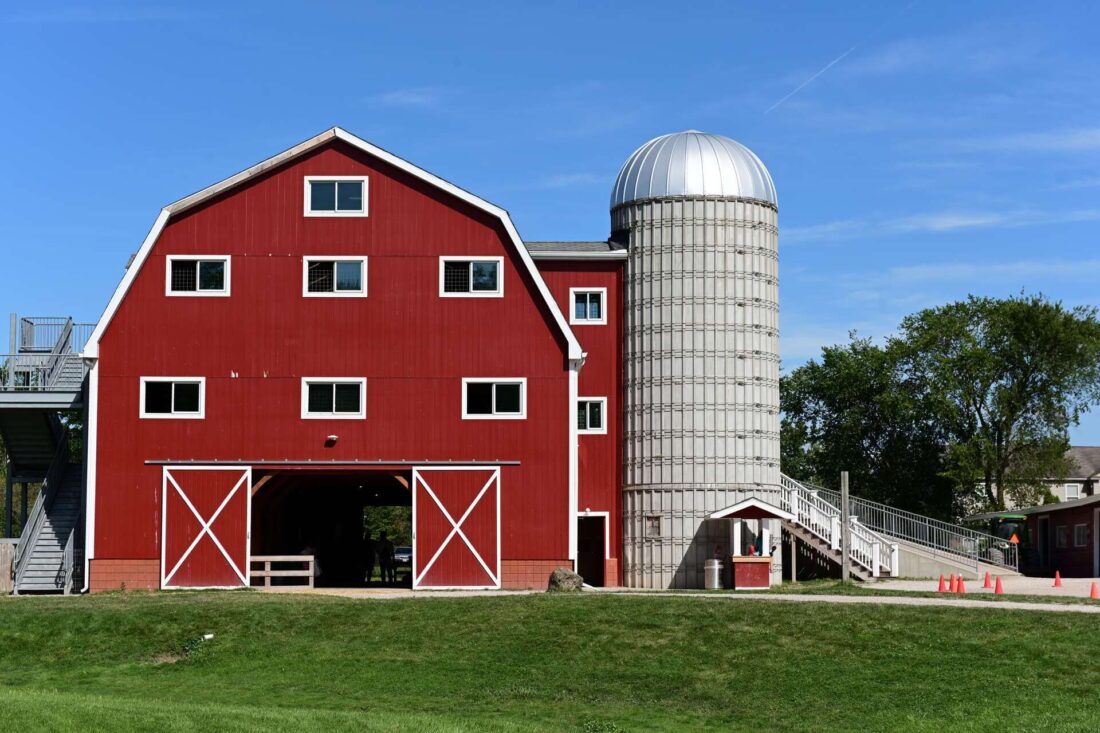 A bright red barn with a silo in a green field