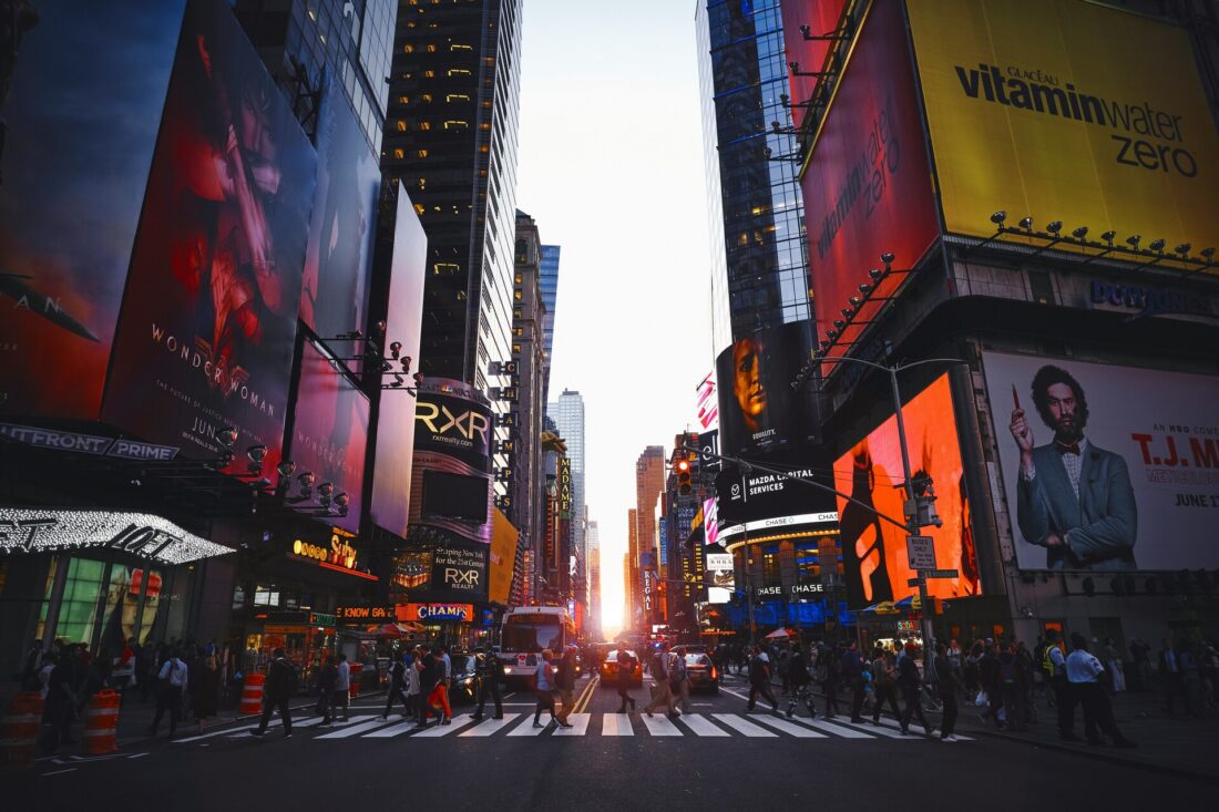 Bustling daytime view of the streets, bright billboards, and crowds at Times Square in New York City.