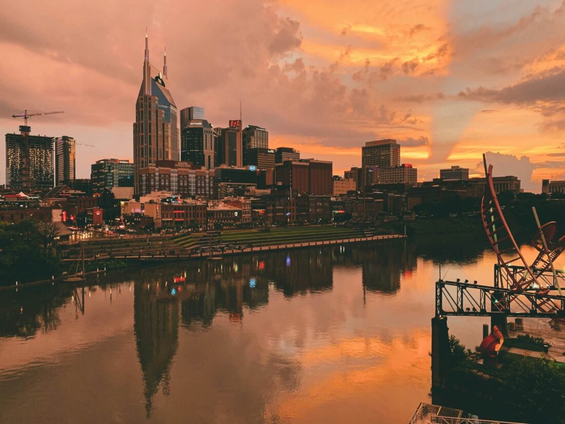 Downtown Nashville skyline reflected on the Cumberland River during a vibrant warm sunset.