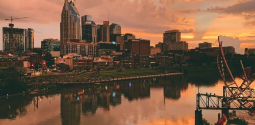 Downtown Nashville skyline reflected on the Cumberland River during a vibrant warm sunset.